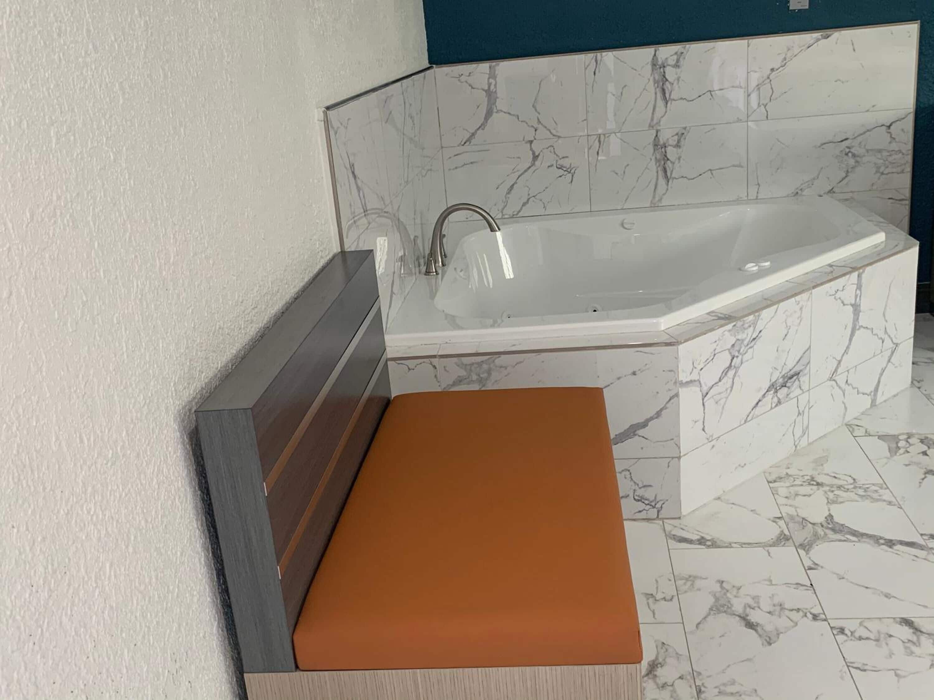 A modern bathroom with a marble-tiled floor, a white bathtub, and a wooden bench with a brown seat.