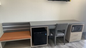 Ein moderner, kompakter Arbeitsbereich mit Schreibtisch, zwei Stühlen, einer kleinen schwarzen Ablage und einem an der Wand befestigten Fernseher.
