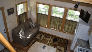 Interior acolhedor de uma cabana, com sofá, mesa de jantar e cozinha.