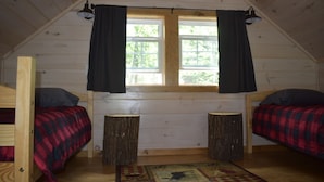 Uma cabana pequena com duas camas, uma janela com cortinas, piso de madeira e um tapete.