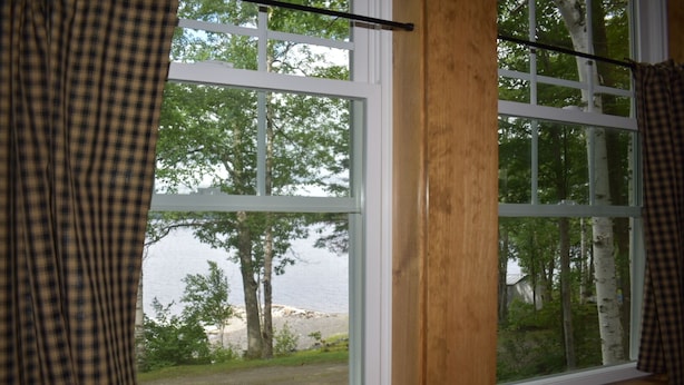 Janela com vista para um lago e árvores, cortinas e moldura de madeira.