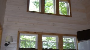 Interior de cabana com área de jantar, ventoinha no teto e grandes janelas.