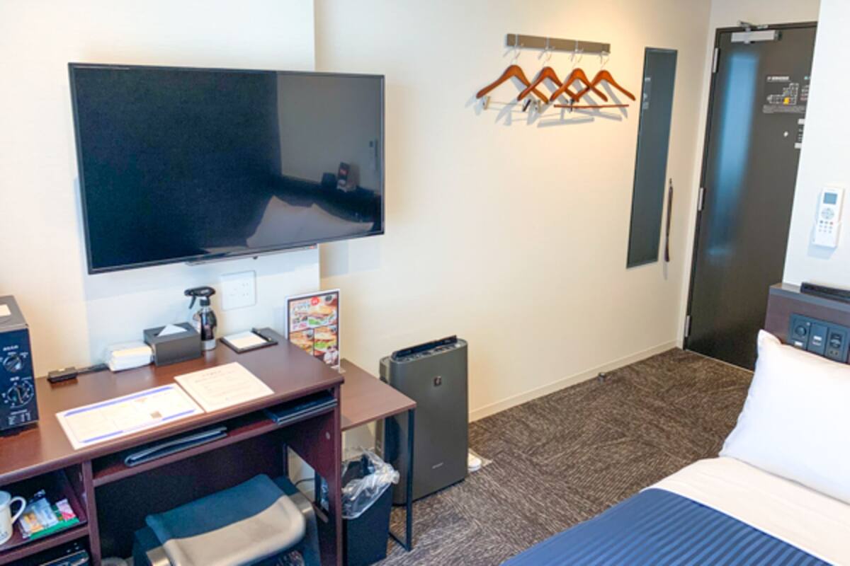 Habitació d'hotel amb un llit, una taula de treball amb un ordinador, una televisió, una perxa per a abrics i un frigorífic.
