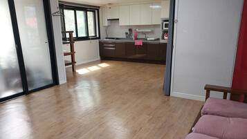 A spacious living area with a wooden floor, a pink sofa, and a kitchen with white cabinets and a microwave.