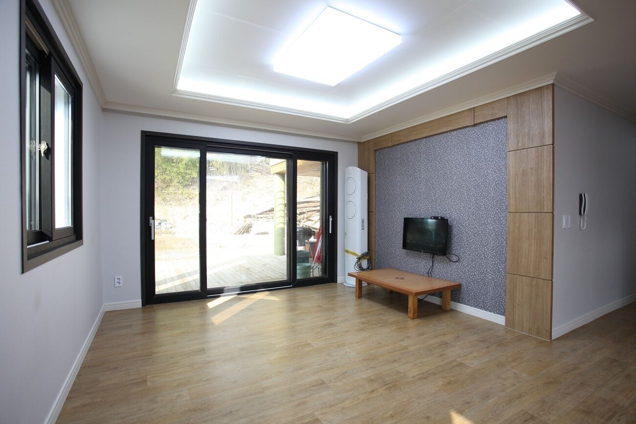 Ein modernes Zimmer mit Oberlicht, einer Glastür und einer Sitzbank, sowie einem an der Wand montierten Fernseher.