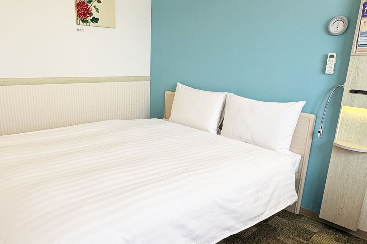 Ein Hotelzimmer mit einem Bett, einer Wanduhr und einem Nachttisch mit Lampe.