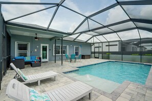 A covered outdoor swimming pool area with lounge chairs, a table, and a ceiling fan.