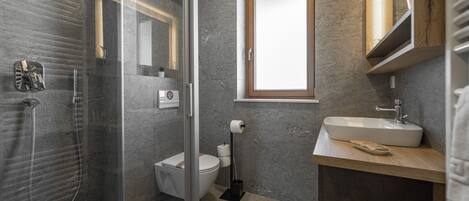 A modern bathroom with a glass shower enclosure, a toilet, and a sink with a wooden countertop.