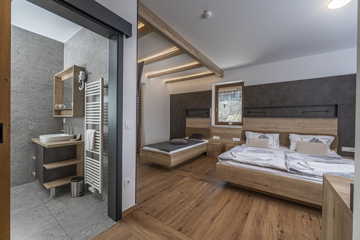 A modern bedroom with a wooden bed, a built-in bench, a small bedside table, and a large window with a view.