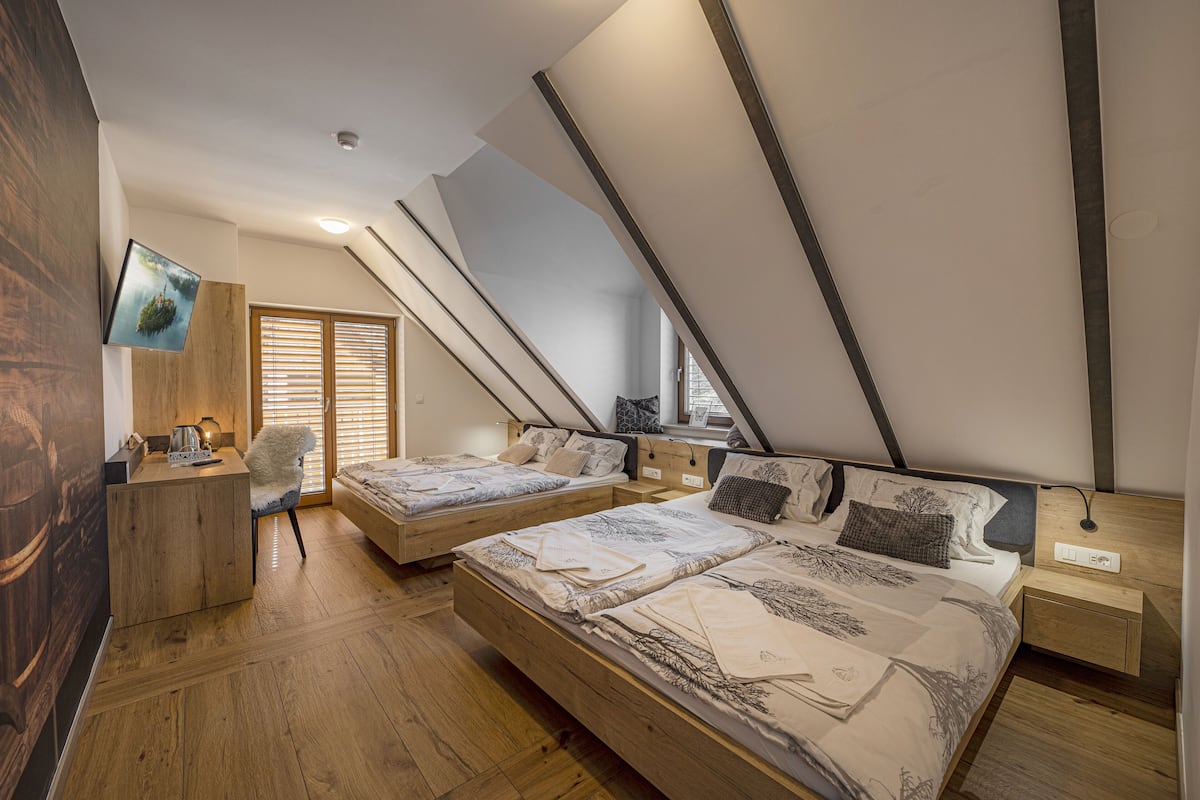 A bedroom with two beds, wooden flooring, a TV on the wall, and a window with blinds.
