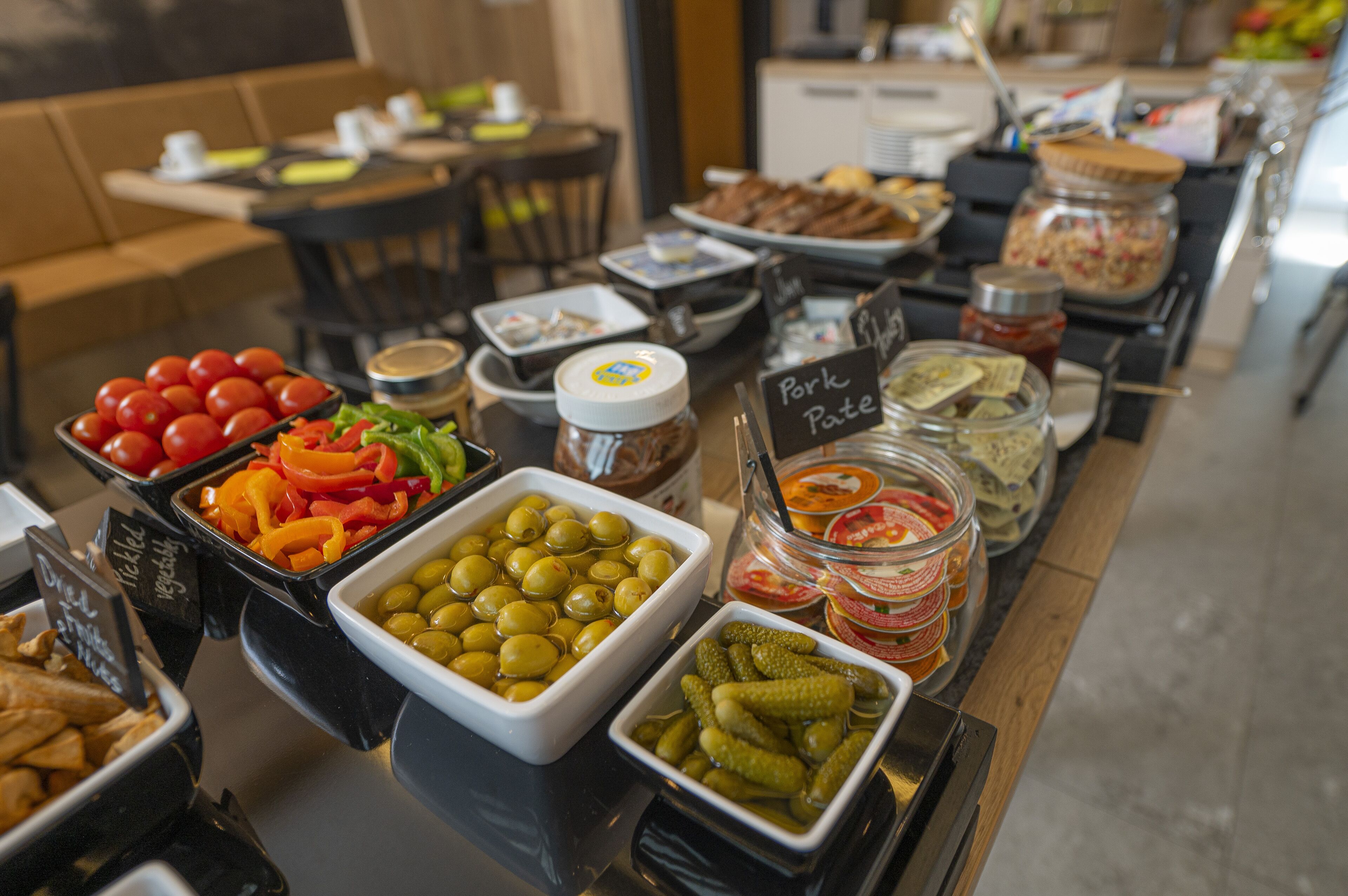Un bufé con diversos alimentos, entre ellos verduras en escabeche, aceitunas y frascos de salsas.
