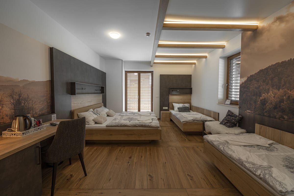 A modern bedroom with a wooden floor, a desk with a chair, two beds, and a large painting on the wall.