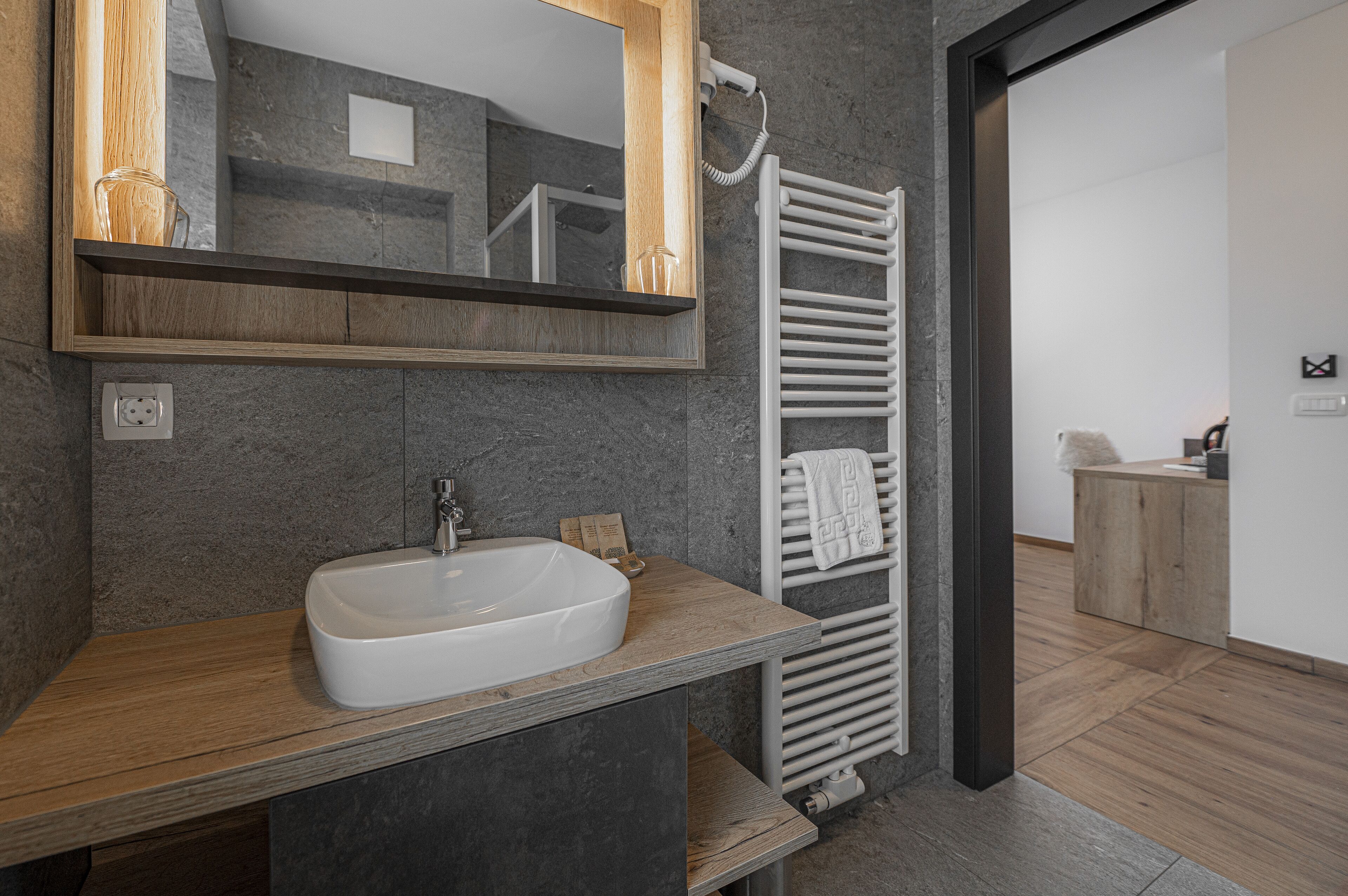 A modern bathroom with a large sink, a mirror, a towel rack, and a wooden vanity.