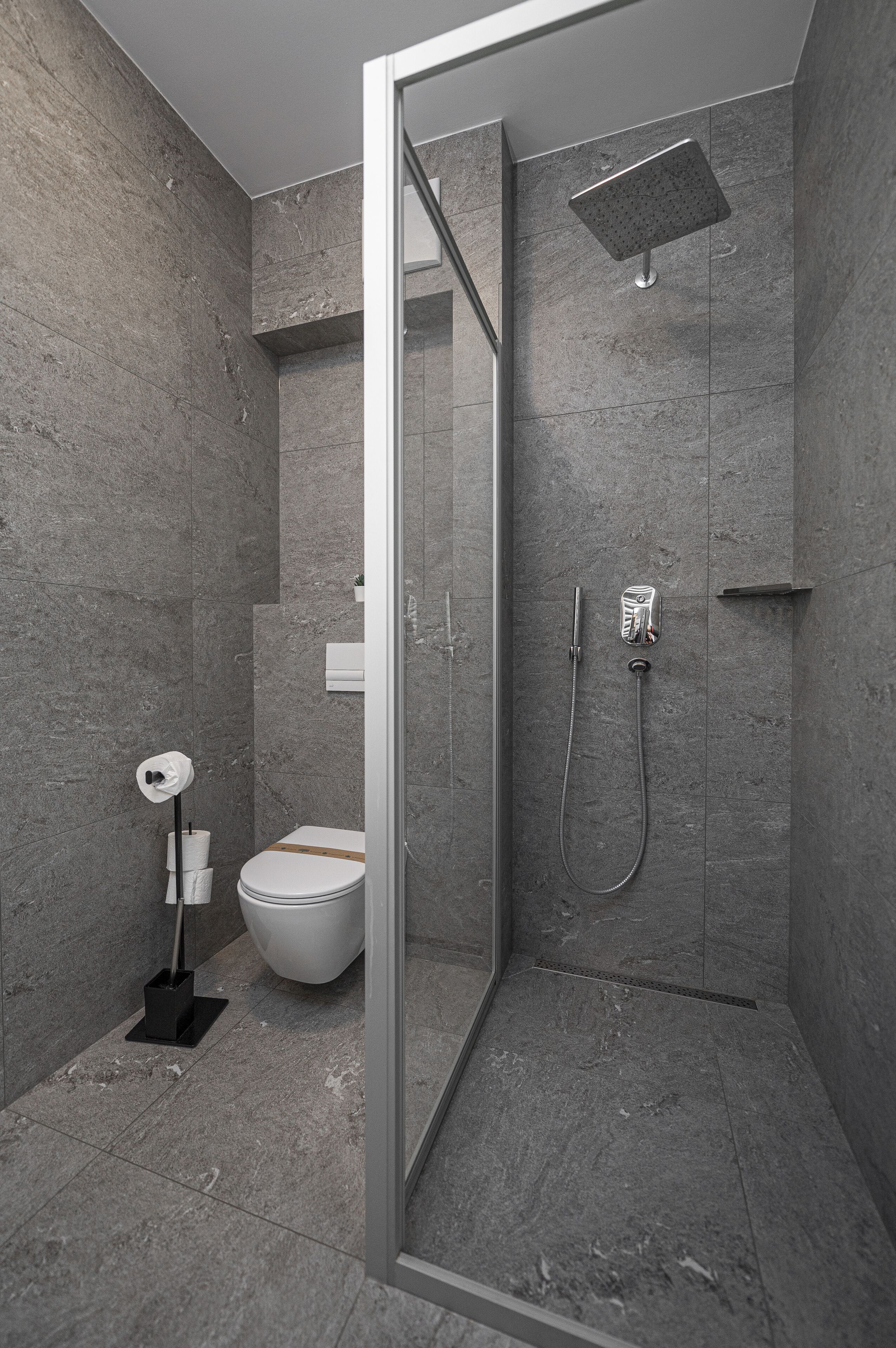 A modern shower area with a glass door, a handheld showerhead, and a wall-mounted control panel.