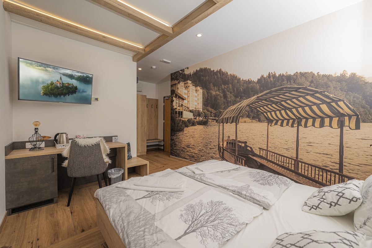 A bedroom with a bed, a desk, and a chair. There is a painting on the wall and a mural of a beach scene.