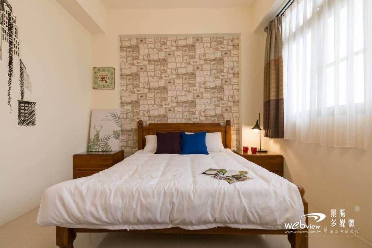 A neatly made bed with a white duvet, a wooden headboard, and a patterned wall behind it.