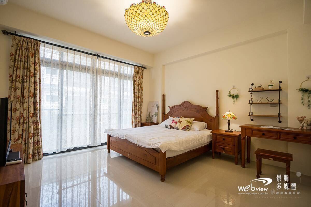 A bedroom with a wooden bed, a desk, a chair, and a lamp.