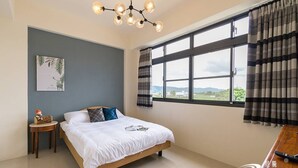 A bedroom with a bed, a small table, a chair, a window with curtains, and a ceiling light fixture. - Wild Fun Hualien (Ji'an)