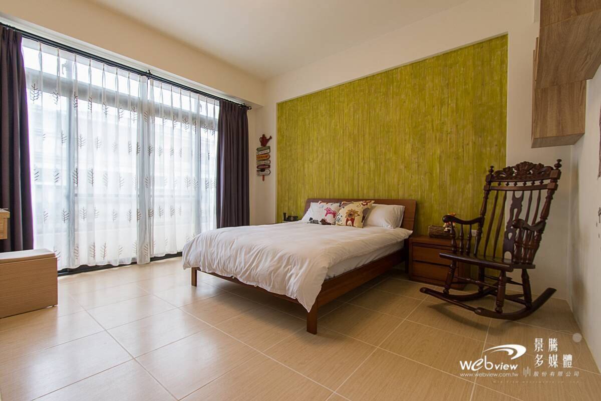 A bedroom with a bed, a rocking chair, a bedside table, and a window with curtains.