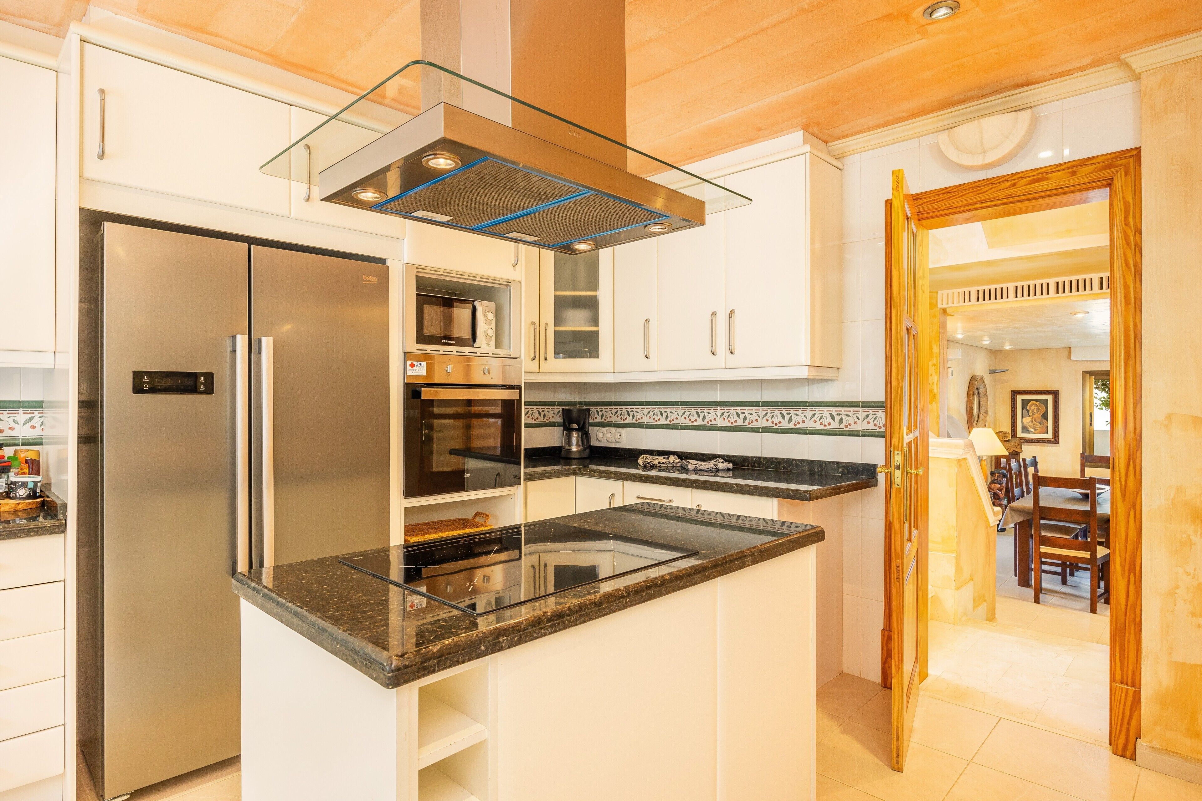 A modern kitchen with a stainless steel refrigerator, built-in oven, microwave, and a glass-enclosed range hood.