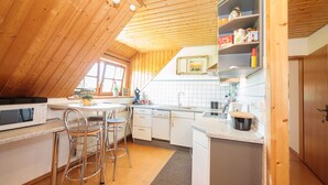 Ett kompakt kök med träpanel i taket, vita skåp, en mikrovågsugn och en diskho.