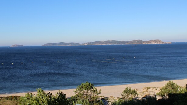 A coastal landscape with a sandy beach, clear blue sky, and distant hills. - Hotel Mar Azul (Sanxenxo)
