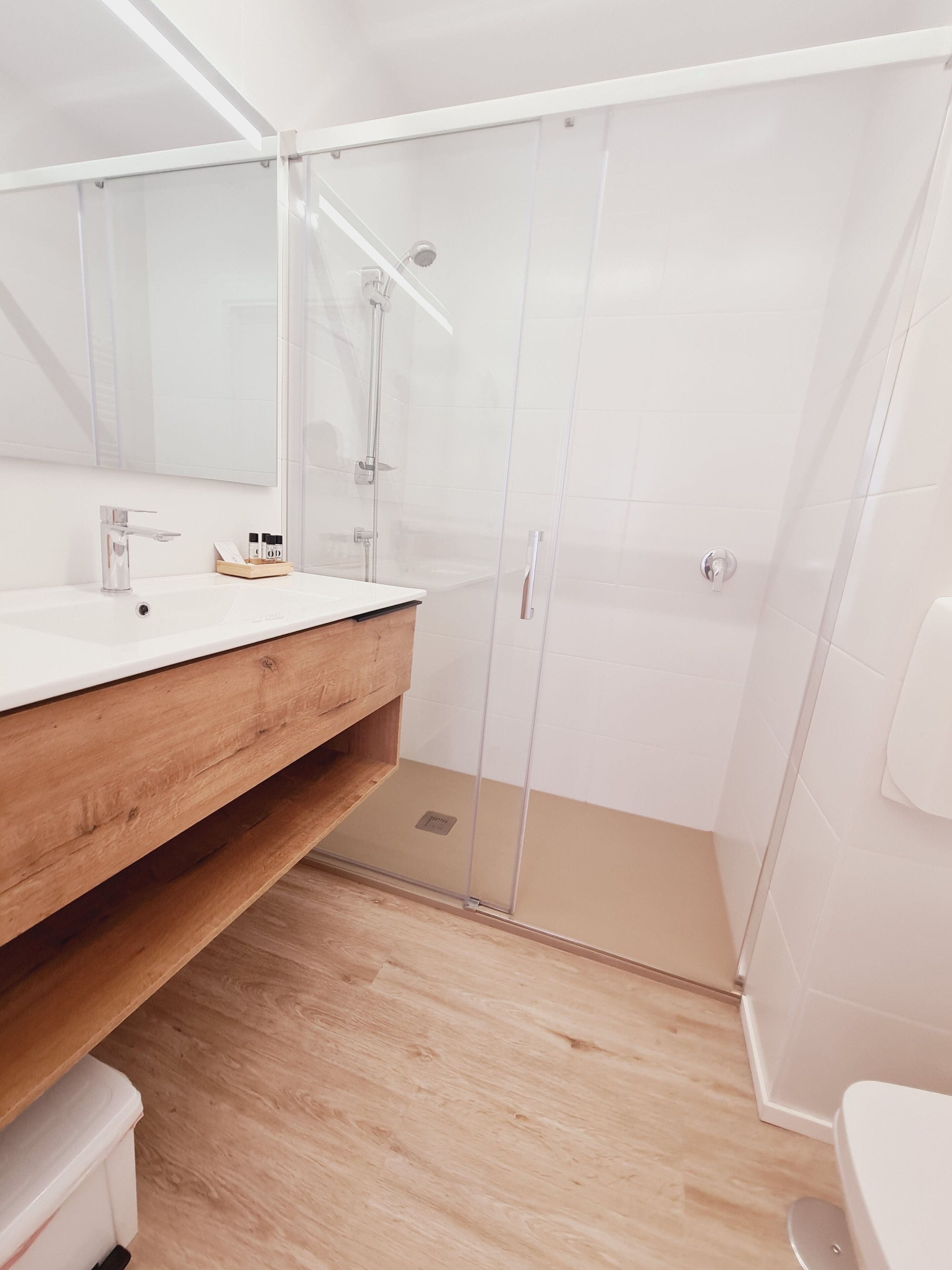 Un baño moderno con tocador de madera, cabina de ducha de vidrio y un inodoro blanco.