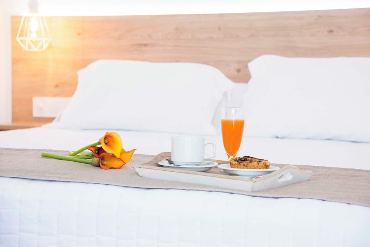 A breakfast tray with a cup of coffee, a glass of orange juice, and a slice of toast on a bed in a hotel room.