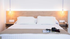A neatly made bed with a wooden headboard, two bedside lamps, a bedside phone, and a camera on the bed. - Hotel Mar Azul (Sanxenxo)