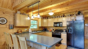 A wooden cabin kitchen with a central island, wooden cabinets, a refrigerator, and hanging pendant lights. - Lakefront Hazelhurst Cabin: Dock & Pool Table (Hazelhurst)
