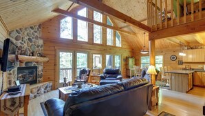 A spacious cabin interior with a stone fireplace, wooden beams, a leather sofa, and a kitchen area. - Lakefront Hazelhurst Cabin: Dock & Pool Table (Hazelhurst)