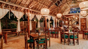Un restaurante con mesas y sillas de madera, luces colgantes y techo de paja.