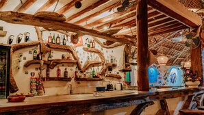 Un rústico espacio de bar con vigas de madera, estantes con varias botellas y un refrigerador azul.