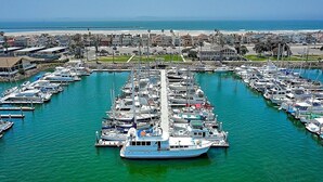 Un puerto deportivo con numerosos barcos amarrados en una disposición simétrica, rodeado de edificios residenciales y una playa al fondo.