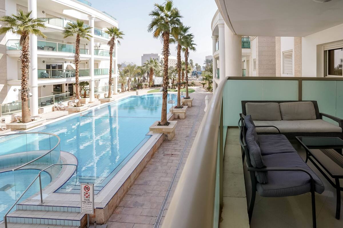 A pool area with a clear pool, lounge chairs, and palm trees.