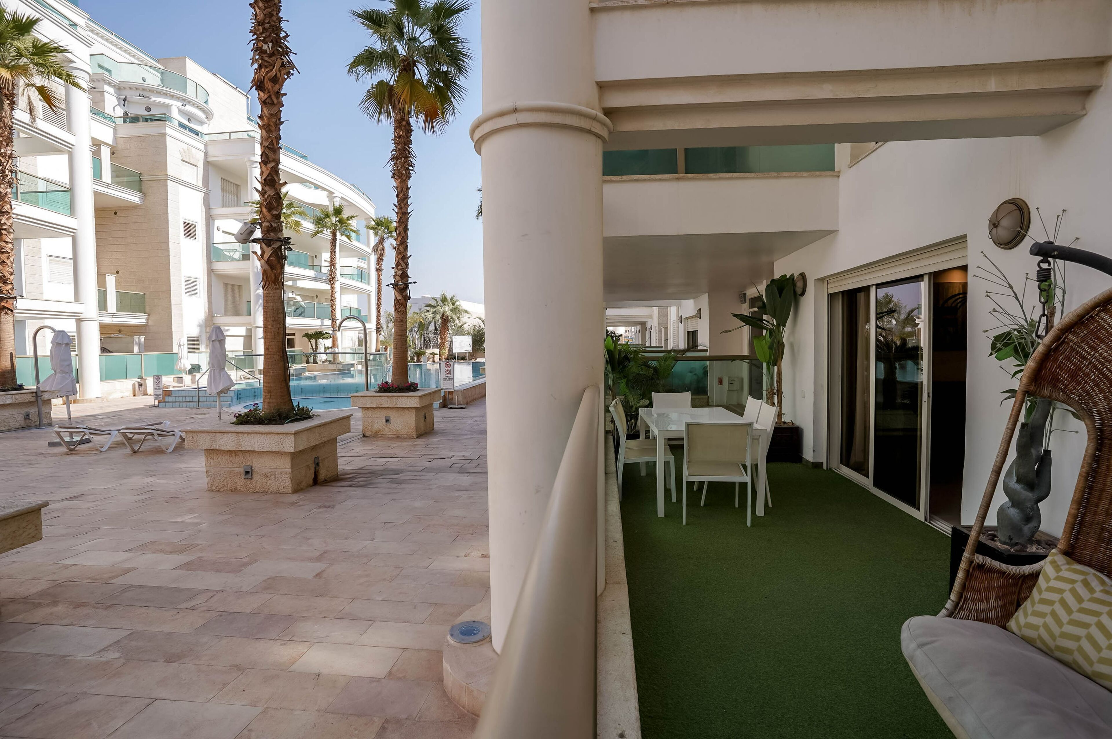 Un patio de hotel con palmeras, mobiliario exterior y zona de piscina.