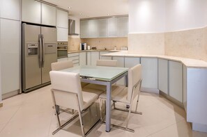 A modern kitchen with a built-in refrigerator, oven, and microwave. There is a glass-top dining table with four chairs. - YalaRent Palmore Resort apartments (Eilat)