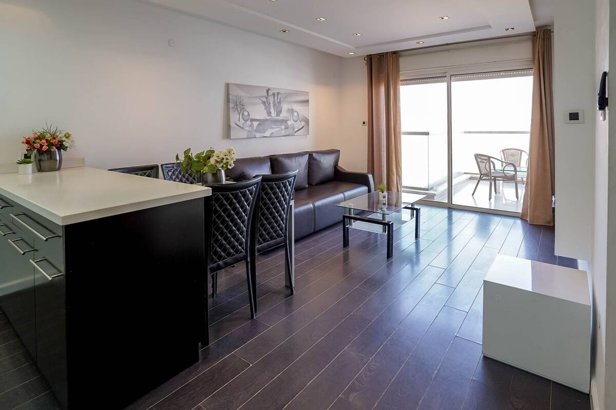 A modern living space with a kitchen area, a sofa, a coffee table, and a balcony with chairs.