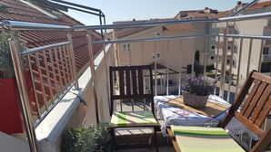 A balcony with a wooden chair, a small table with a tablecloth, and potted plants. - Apartments Adriatic Split-Stobreč (Split)