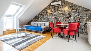 A loft-style room with a stone wall, a dining area with red chairs, a sofa with a blue throw, and a skylight. - Apartments Adriatic Split-Stobreč (Split)