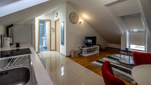 A modern kitchen with a sink and stove, a dining area with a red chair, a television on a white stand, and a clock on the wall. - Apartments Adriatic Split-Stobreč (Split)