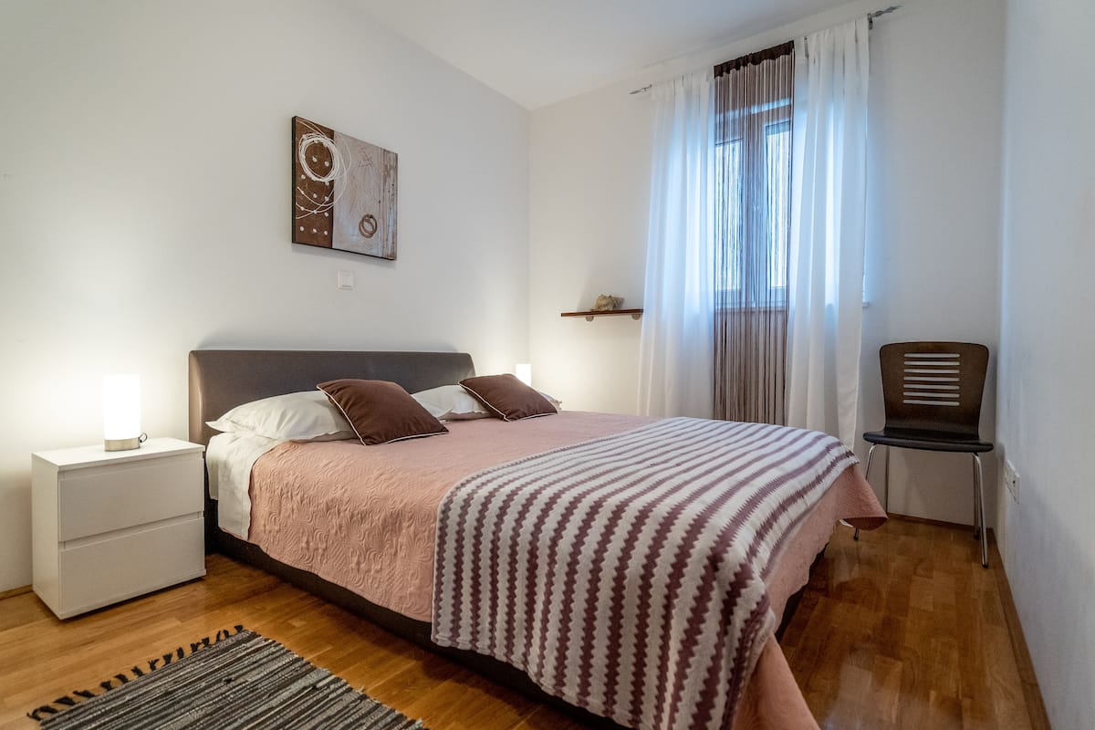Une chambre bien rangée, avec un lit, des tables de chevet, une chaise et une fenêtre avec des rideaux.