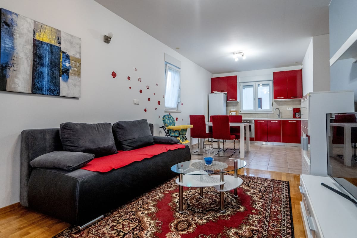 Un salon avec un canapé, une table basse et un tapis. Il y a également un coin cuisine avec des meubles rouges et une table à manger.