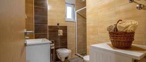A bathroom with a shower, toilet, and a small window.