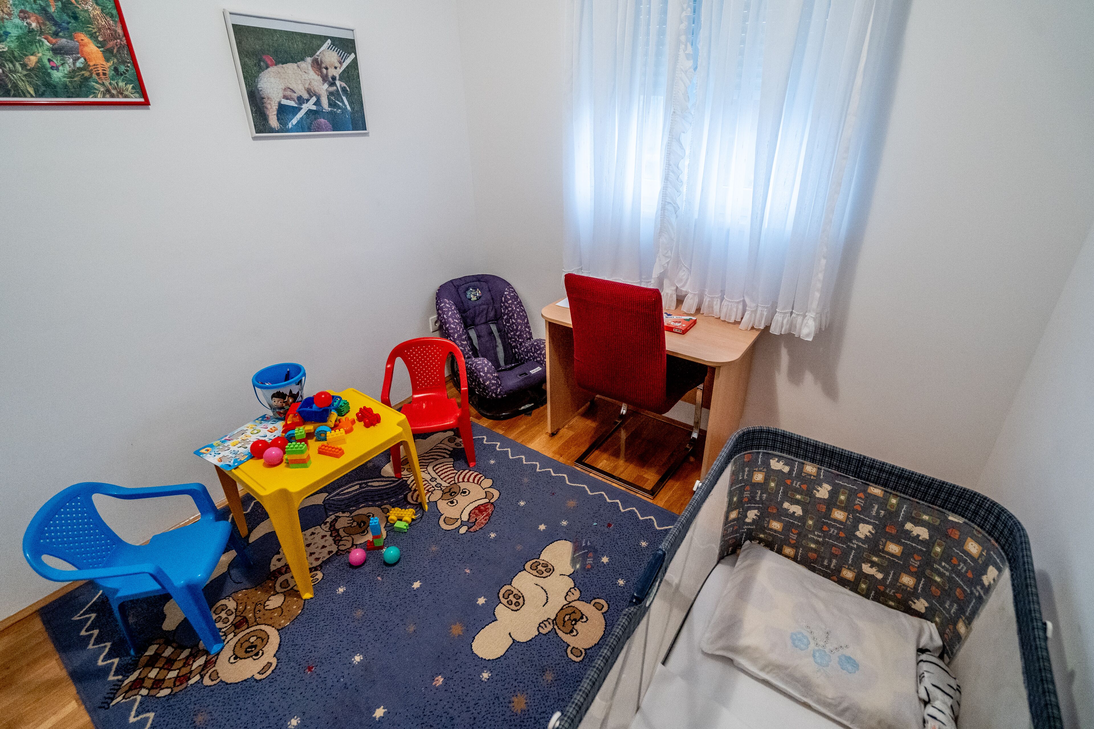 A child's playroom with a blue rug, a small table with toys, a red chair, and a crib.