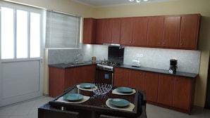 Una cocina compacta con armarios de madera, estufa integrada, un lavamanos y una zona de comedor con una mesa preparada para cuatro.