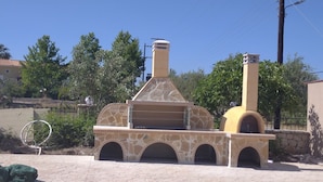 Un horno de piedra al aire libre con chimenea, rodeado de un área empedrada y vegetación.