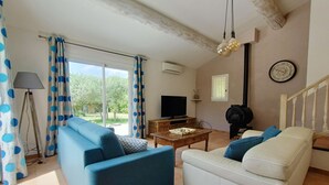 Ett vardagsrum med en blå soffa, en vit soffa, ett soffbord i trä, en tv och en trappa.
