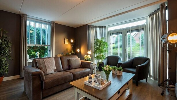 Una sala de estar moderna con un sofá marrón, un sillón negro y una mesa de centro de madera con objetos decorativos.