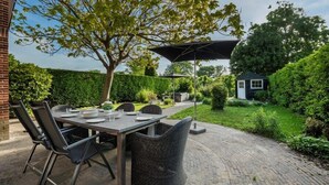Un patio al aire libre con una mesa lista para comer, rodeada de sillas y una sombrilla grande que da sombra.